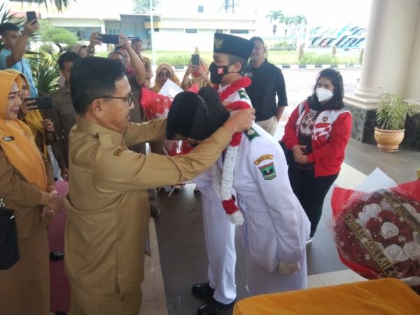 Bupati Solsel Khairunas mengalungkan bunga kepada Faiha Athahillah, seorang siswa asal Solok Selatan yang membawa Sang Saka Merah Putih di Istana Negara, Senin (29/8/22) di BIM (IST)